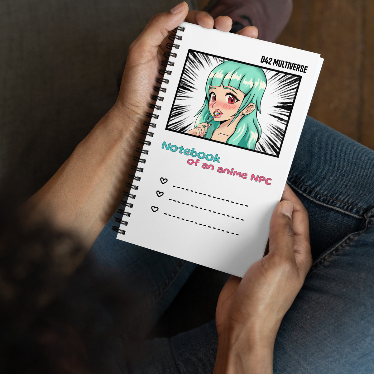 Weißes D42 Spiralnotizbuch mit Manga-inspirierter Illustration eines türkishaarigen Anime-Charakters und dem Schriftzug „Notebook of an anime NPC“ in der Hand gehalten